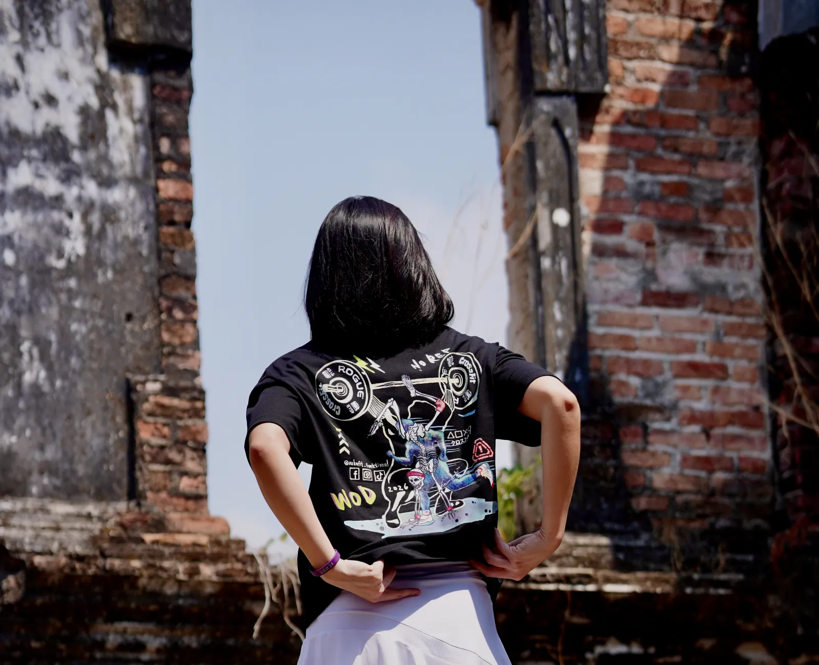 Kareen seen from behind in a graphic tee, framed by brick ruins