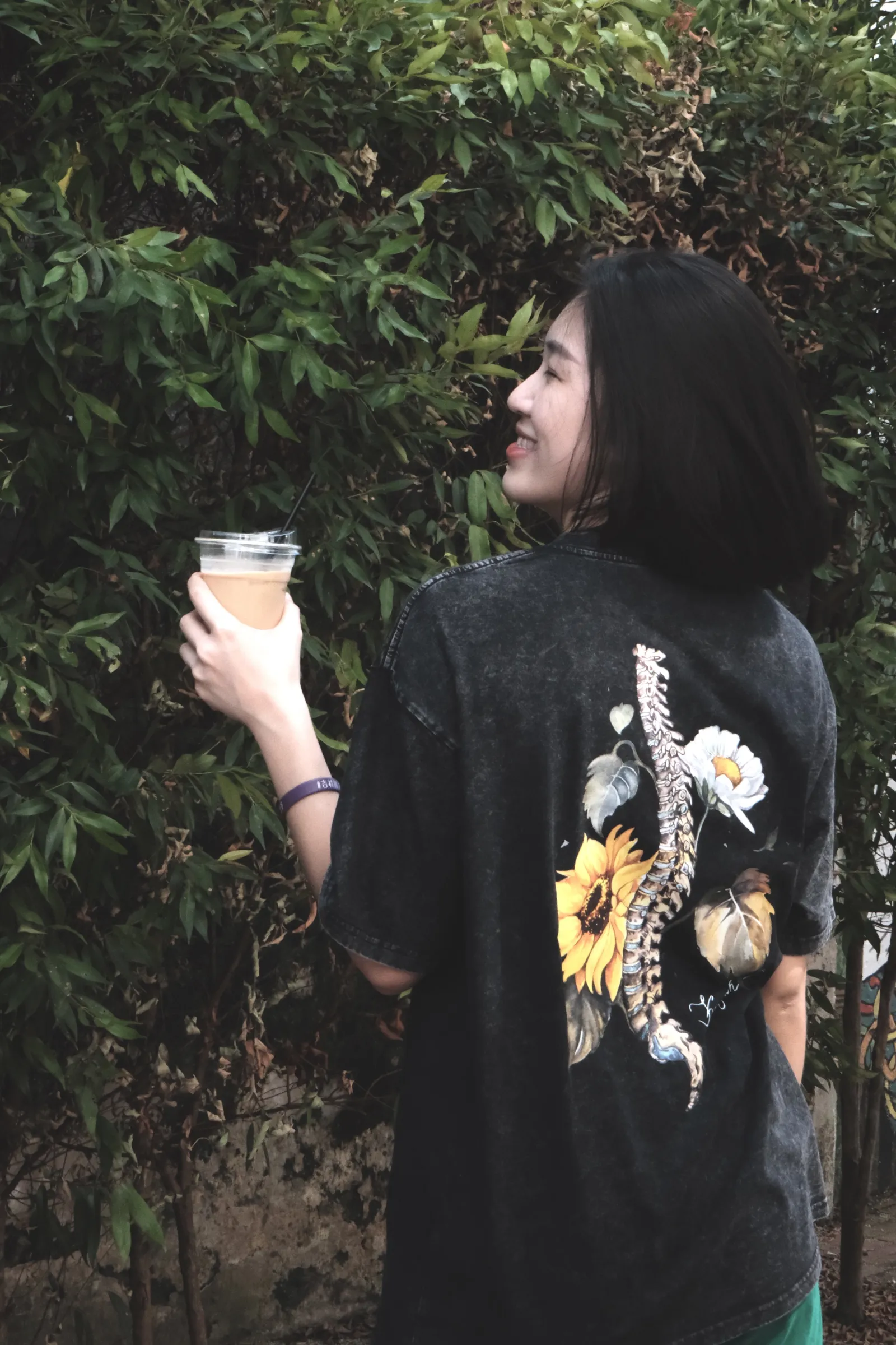 Kareen outdoors in a floral graphic tee, holding an iced drink